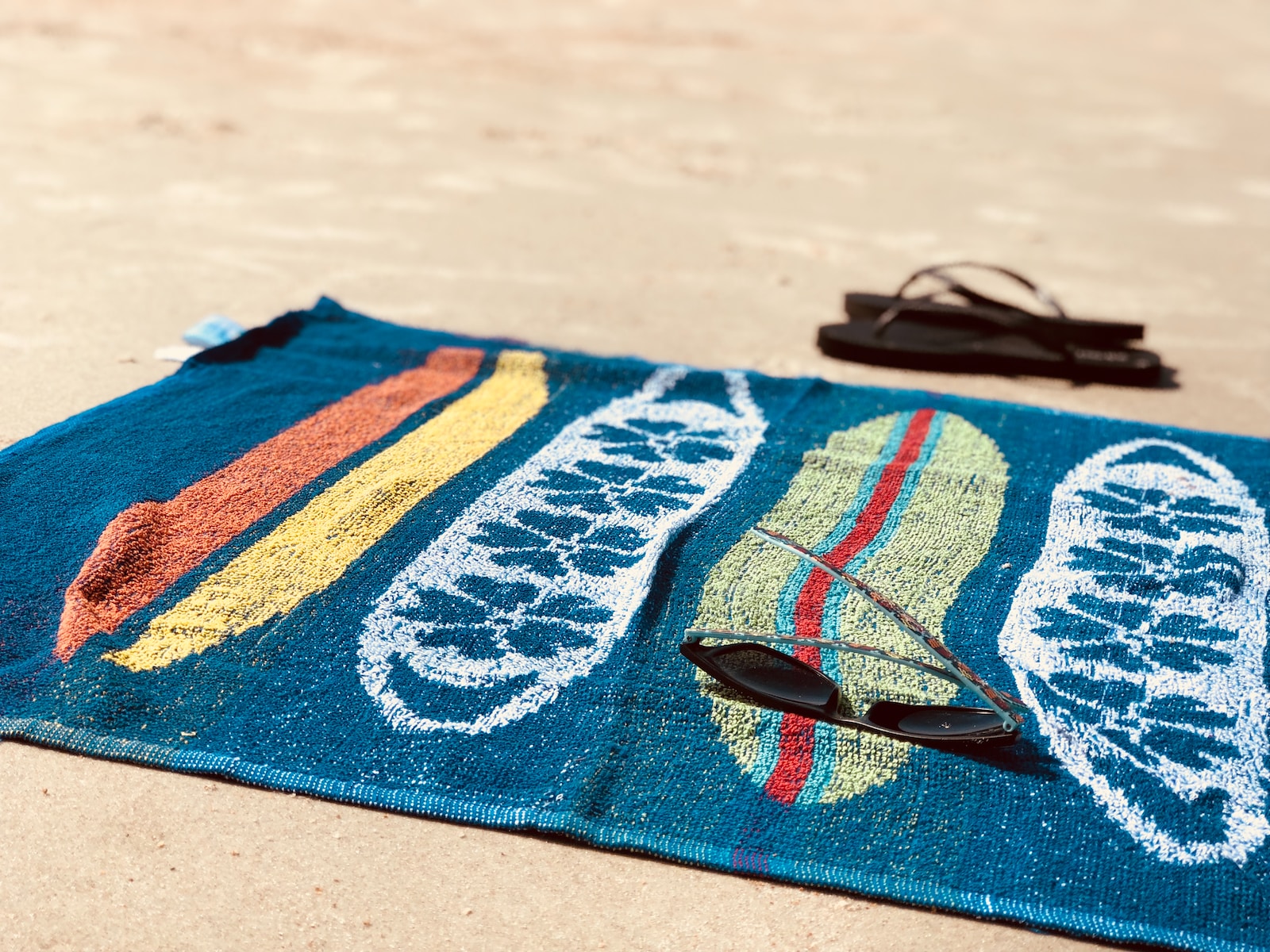black sunglasses on blue towel beside pair of black flip-flops